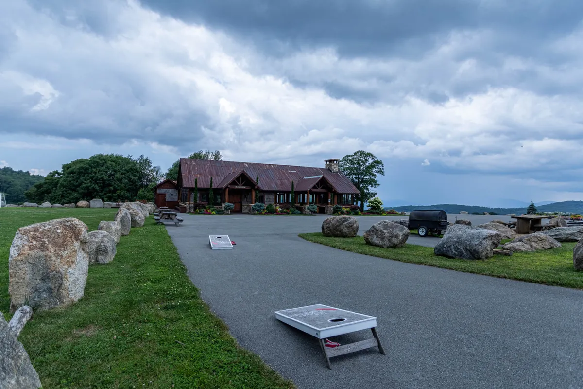 An exterior view featuring a rustic lodge surrounded by large rocks, cornhole boards set out for play, and a relaxed outdoor area that encourages group activities and friendly competition.