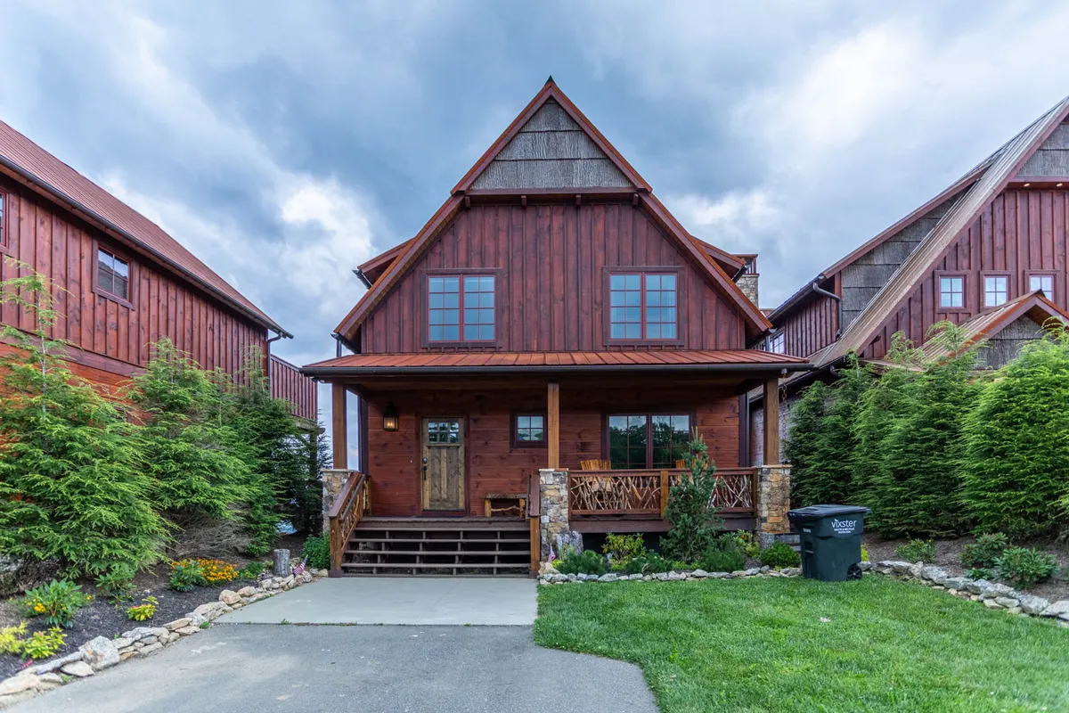 The image showcases the exterior of Sunrise Lodge, highlighting its charming wooden facade, a spacious and inviting porch perfect for gatherings, and a beautifully landscaped garden. The scene is set during the golden hour, emphasizing cozy sunset views and the welcoming atmosphere of this mountain home.