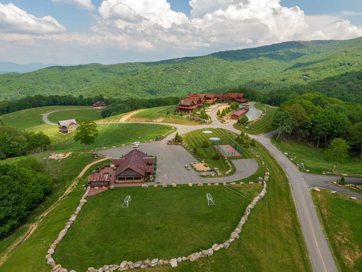 The main lodge sits nestled in a picturesque mountain setting, with recreational areas and gathering spaces visible. Families and groups can be seen enjoying outdoor activities, emphasizing the inclusive community atmosphere and access to amenities.