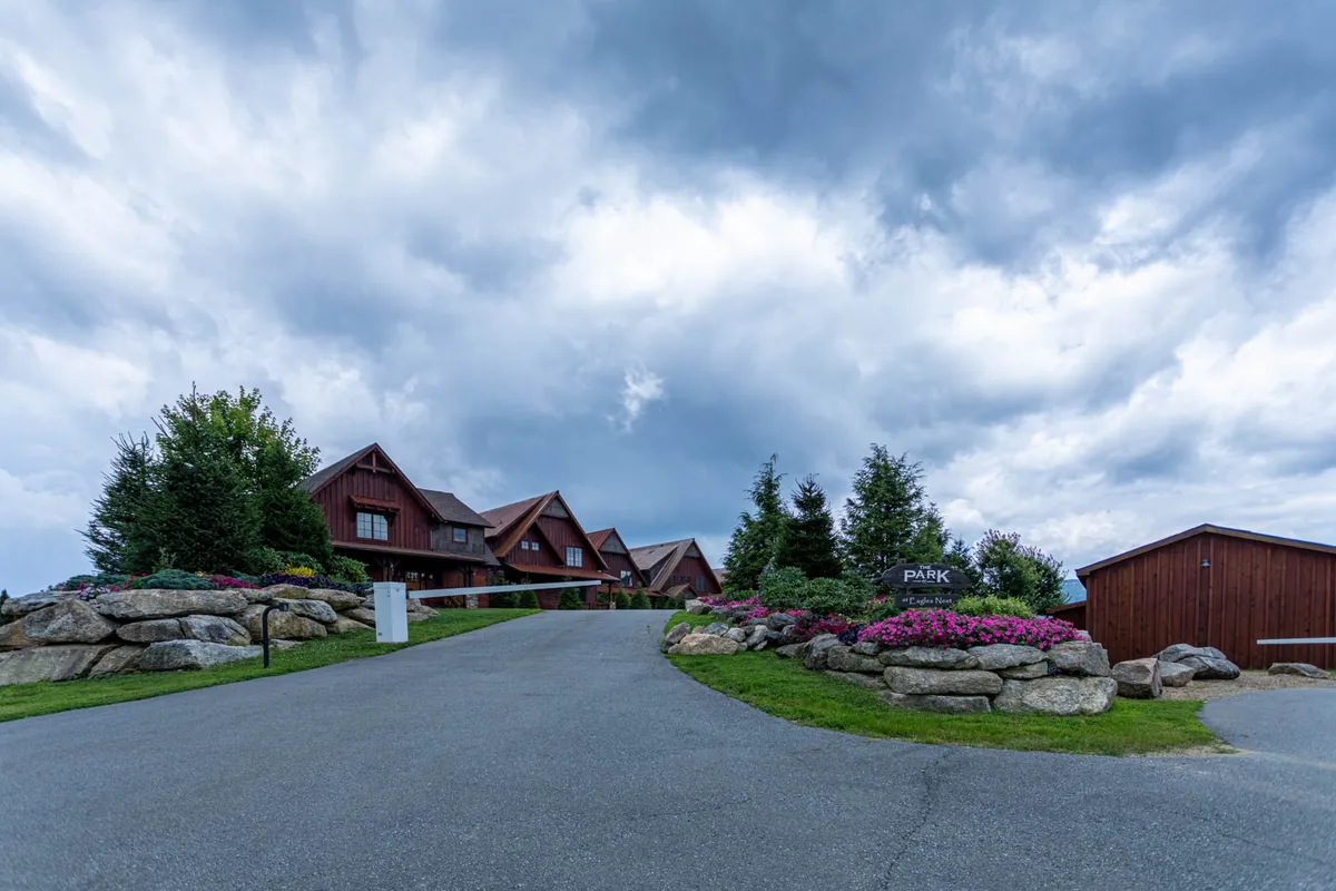 This image presents the main lodge with a rustic design surrounded by vibrant flower beds and stone landscaping. The exterior feels inviting and well-maintained, offering clear sightlines to natural spaces ideal for pets. The scene suggests ample outdoor areas for walking, play, and relaxation, reflecting a welcoming environment for guests and dogs alike.