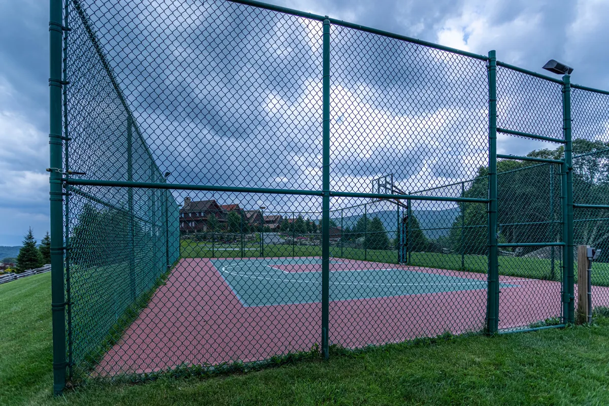 A well-maintained tennis court surrounded by lush greenery and distant houses creates a vibrant hub for outdoor sports and social gatherings. The scene hints at the possibility of sunset matches and community tournaments.