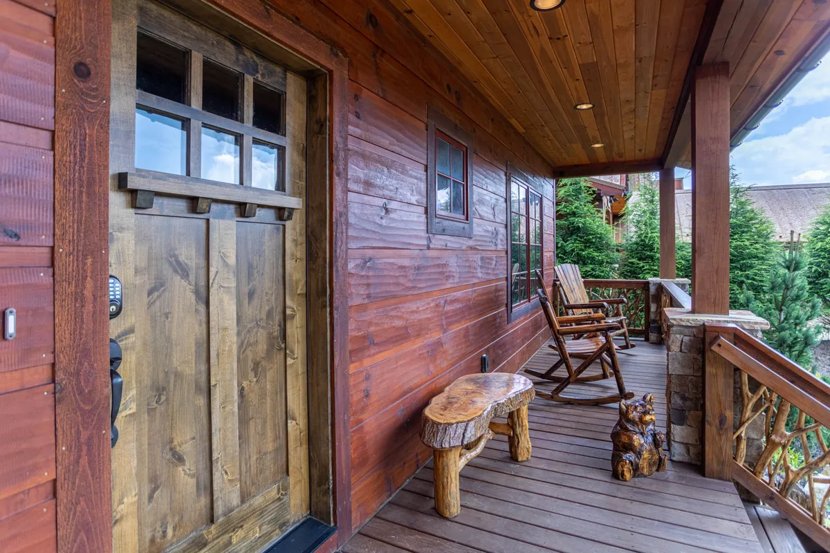 A cozy exterior scene featuring a wooden door, rocking chairs, a wooden bench, and a decorative bear statue on the porch. The inviting front area is perfect for relaxing while pets lounge nearby or enjoy the fresh mountain air, and the design subtly reinforces the lodge’s friendly, homey appeal.
