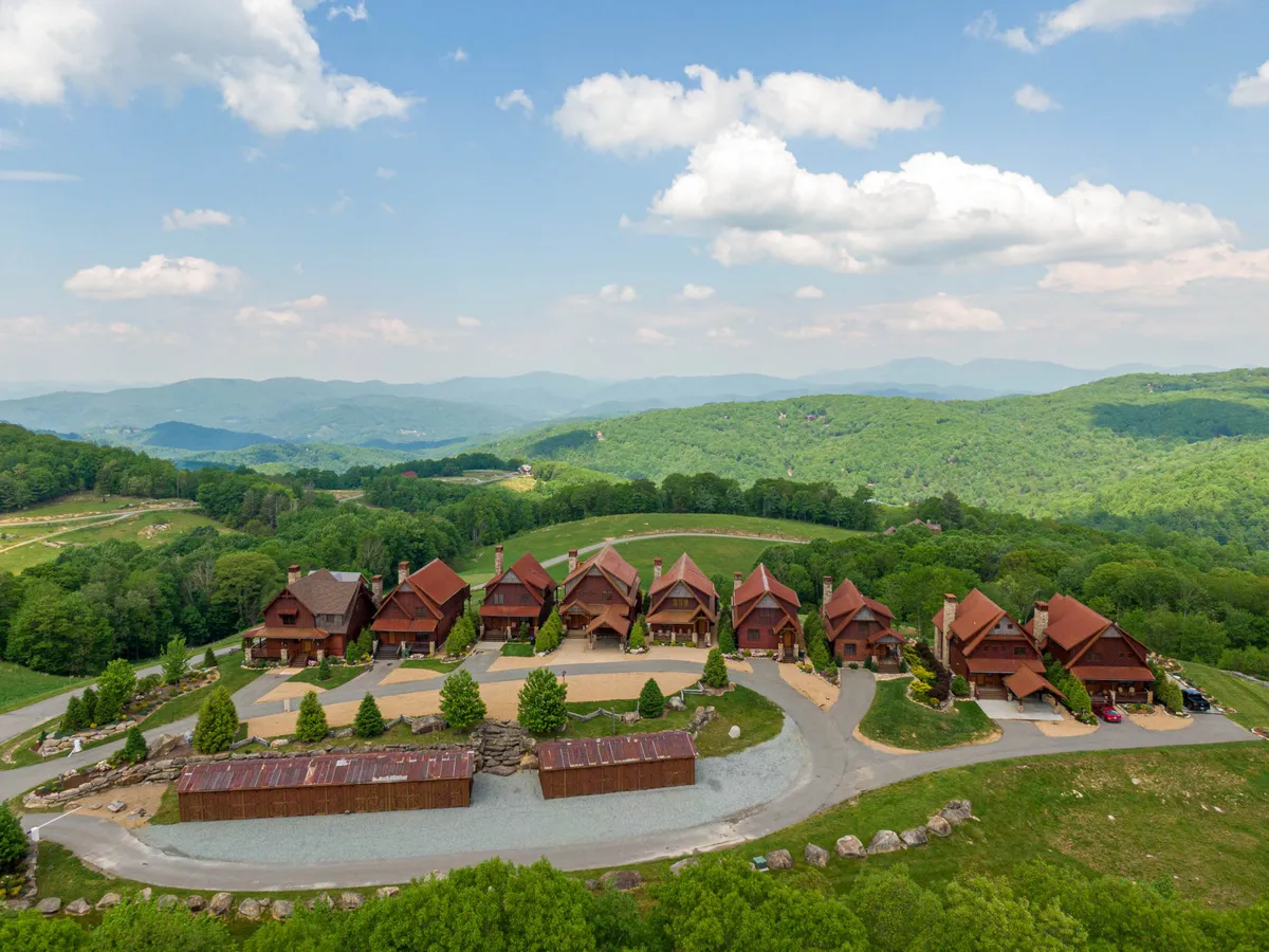 A row of rustic cabins nestled among lush greenery with a majestic mountain backdrop and a circular driveway, inviting families to gather and explore the outdoors together.