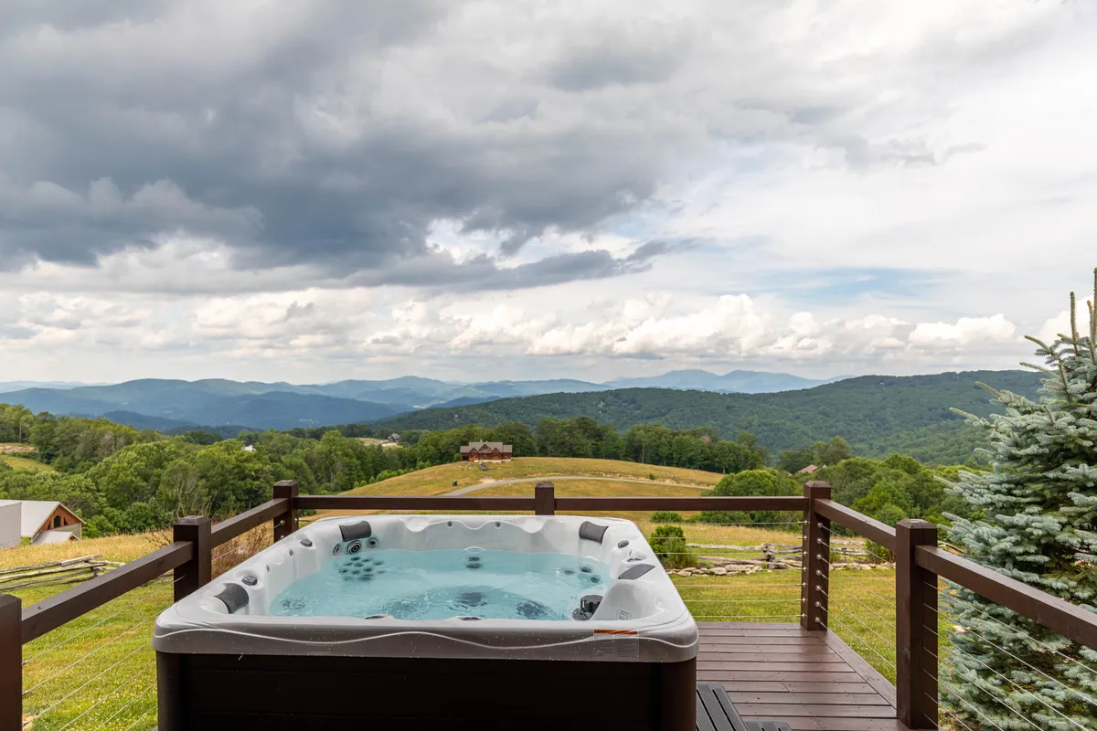 A serene exterior shot showing a hot tub on a deck with a panoramic mountain view and sturdy deck railing, perfect for relaxation after a day of adventure.