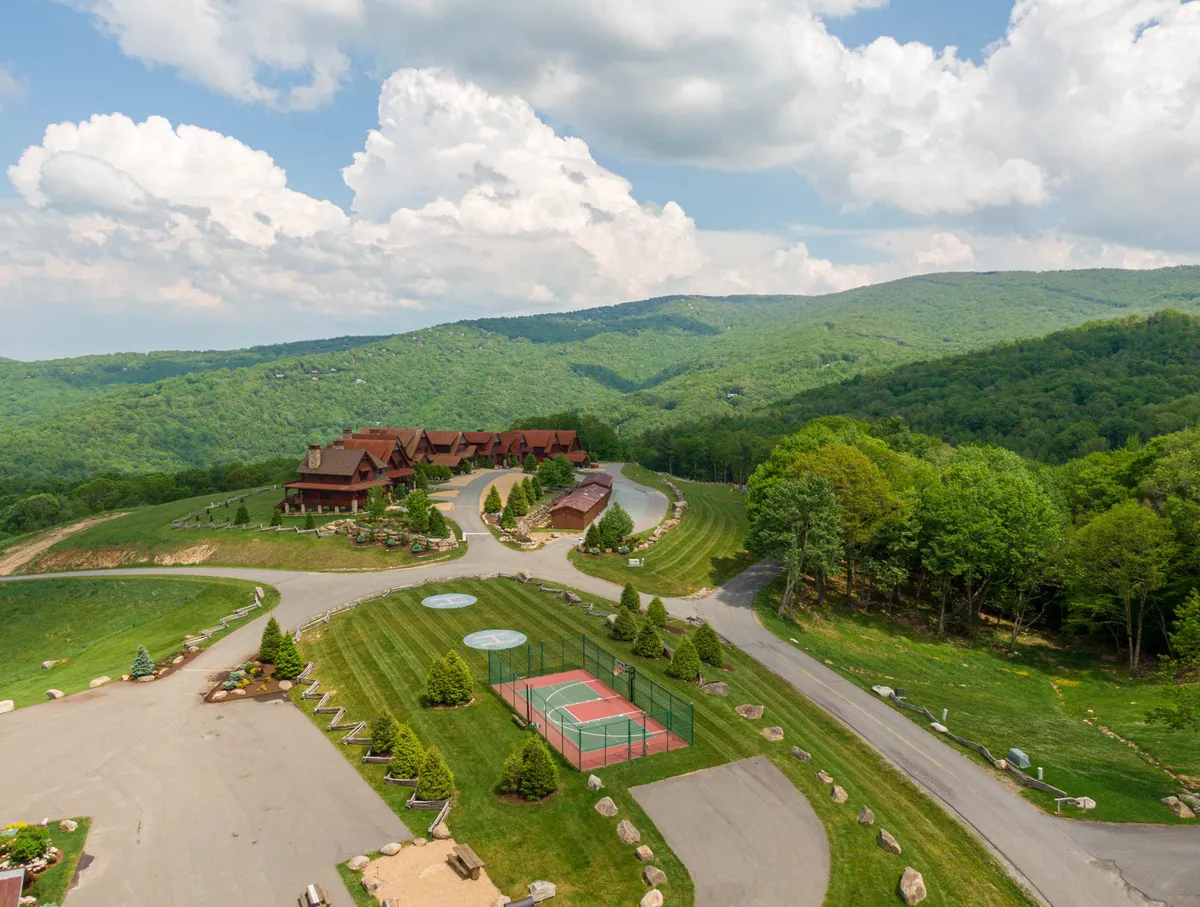 An exterior view of the Eagles Nest community featuring a sweeping mountainous landscape, well-maintained lawns, a prominent tennis court, and wooden lodges. The scene is set in daylight, with lush greenery and inviting outdoor facilities.