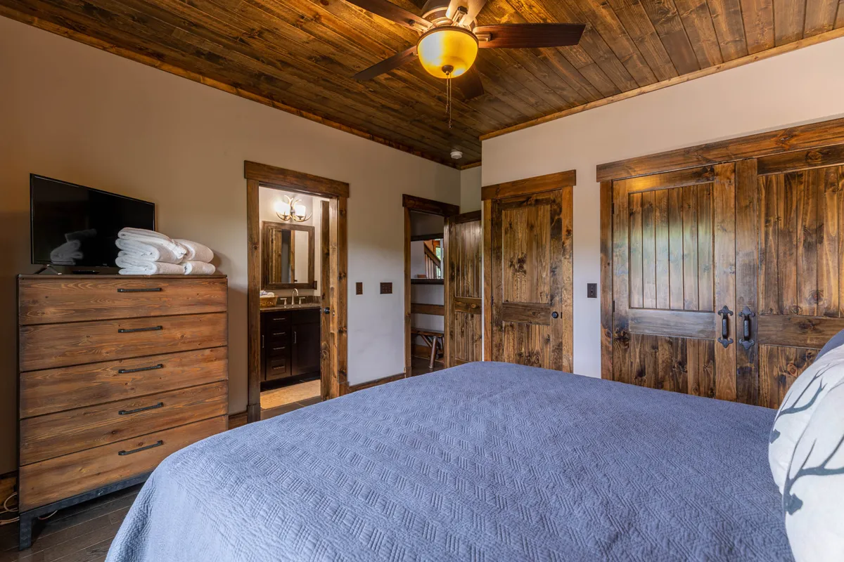 A warm and inviting guest space with a bed covered in soft, textured linens, a wooden dresser, and classic wooden doors. The gentle morning light adds to the restful atmosphere, making it ideal for guests or family members seeking comfort.