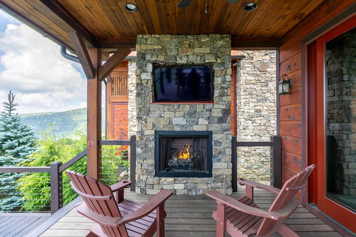A cozy outdoor seating area with wooden chairs faces a beautiful stone fireplace, all set against a backdrop of majestic mountain views. The space is perfect for sharing meals, unwinding by the fire, or simply enjoying the peaceful mountain atmosphere.